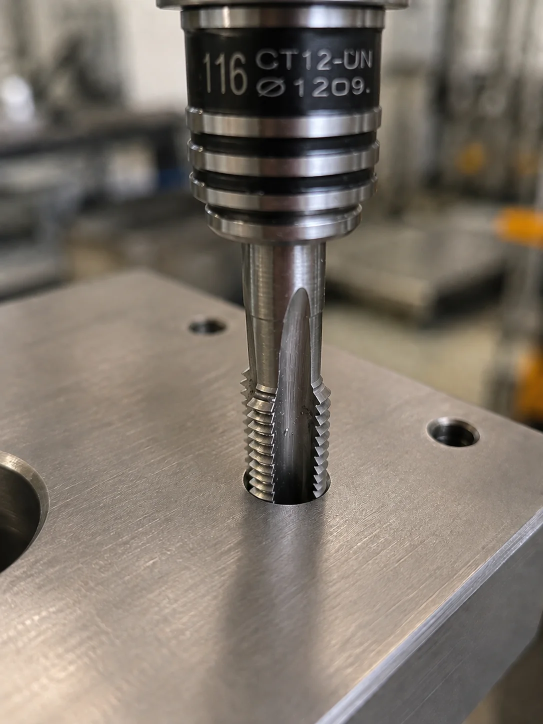 Machine tap cutting an internal thread in a metal plate