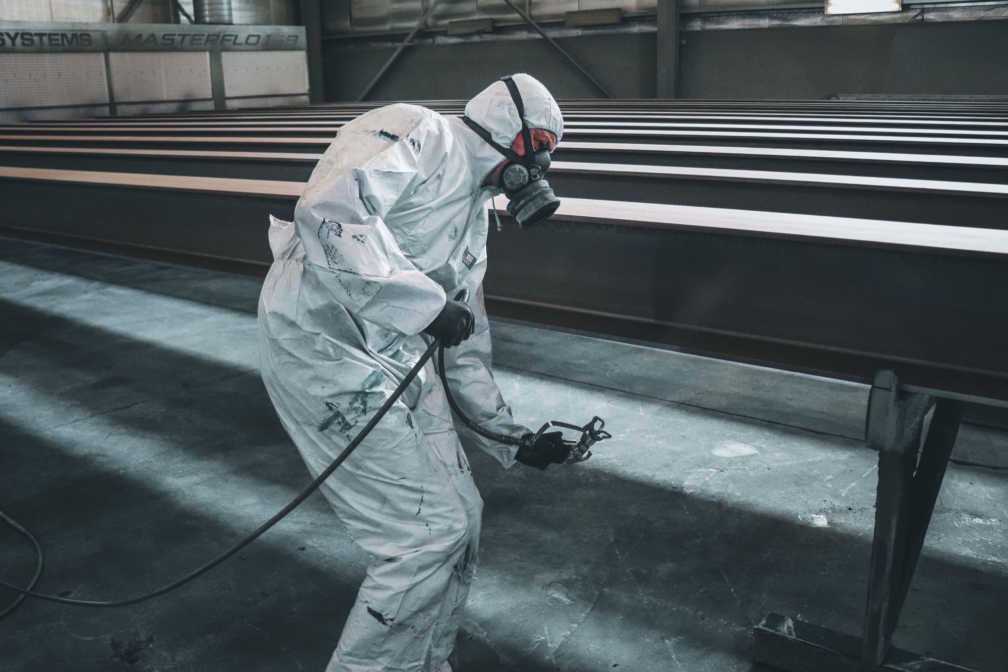 Protected operator spray painting structural metal in an industrial booth